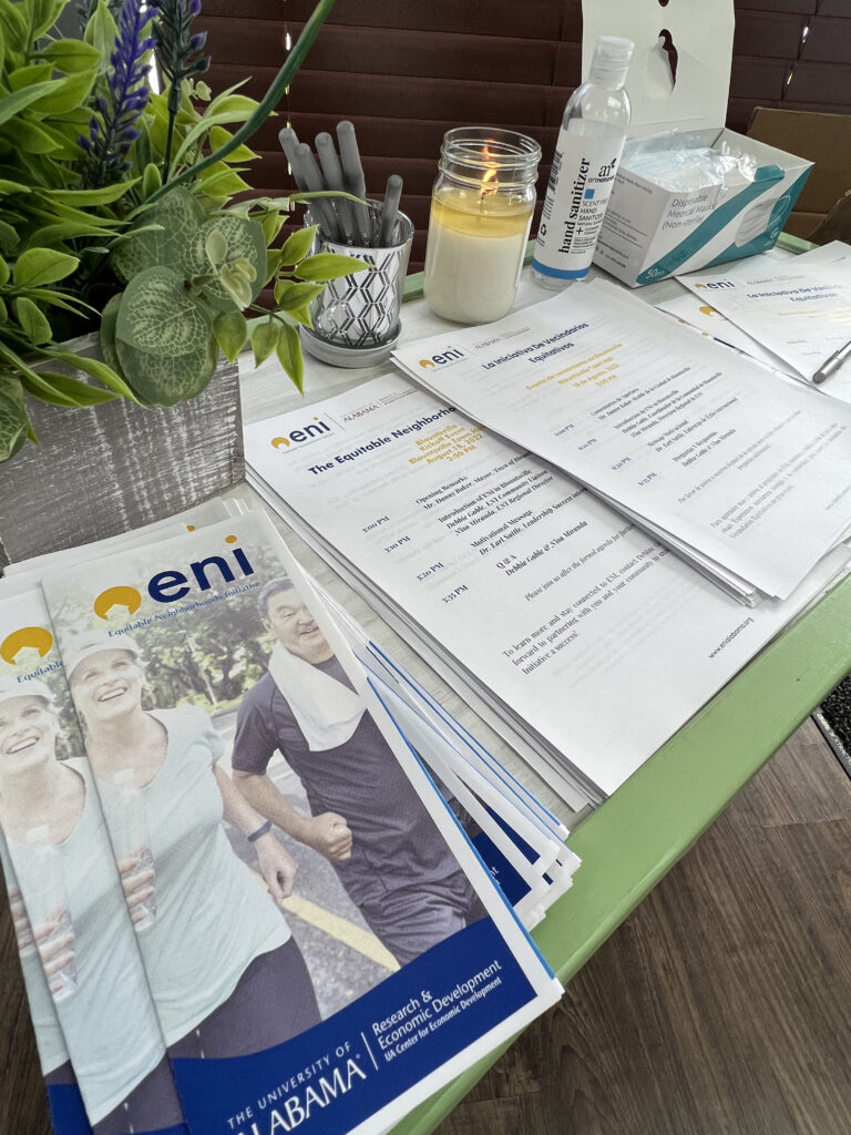 A table displaying ENI brochures as well as kickoff agendas written in both English and Spanish. The table also has pens, hand sanitizer, masks, a  candle, and a plant