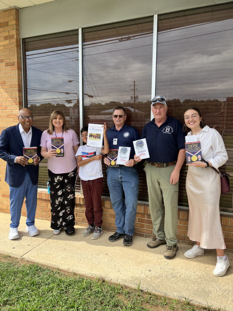 Dr. Earl Suttle stands with community members and ENI team member Erin holding his leadership books in front of Blountsville Town Hall
