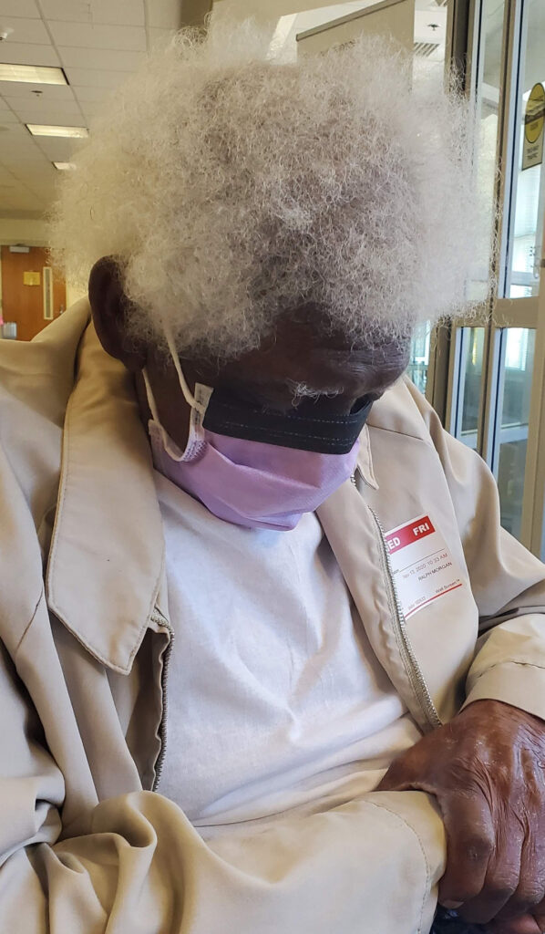 Older gentleman sleeps in a wheelchair wearing a mask