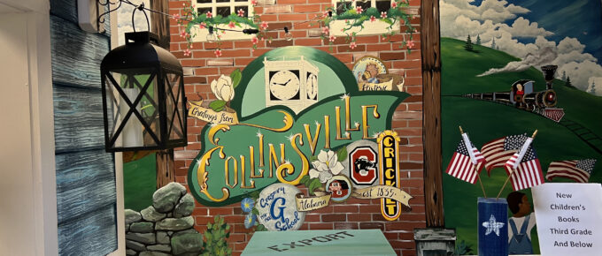 A mural on the wall of the Collinsville library. The mural is painted to look like an old building and rolling hills with a train in the background. On the building, it says "Greetings from Collinsville Alabama." It's essentially a mural of a mural.