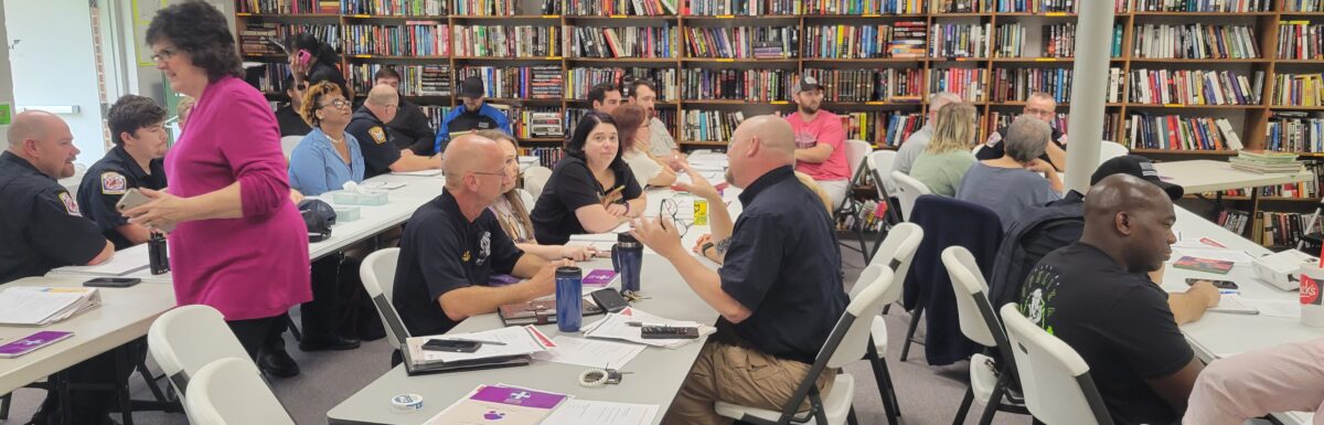 First responders and lay people sit around tables, engaged in small group discussions about Mental Health First Aid.
