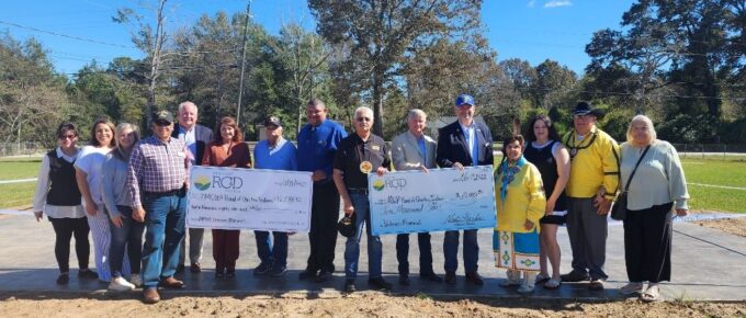 A group of tribal members and RC&D representatives stand with large checks from the RC&D at the Veterans Park ribbon cutting