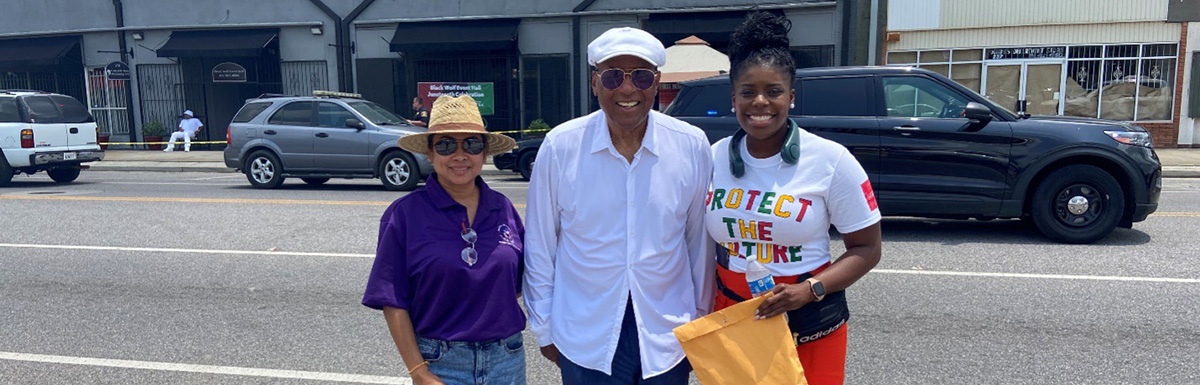 Stephanie Khat, Dr. Earl Suttle, and LaSheryl Dotch pose for a picture on the street in front of some downtown buildings in Prichard. LaSheryl is wearing a t-shirt that says "Protect the Future" and Stephanie is wearing a t-shirt from the Alabama Department of Public Health.