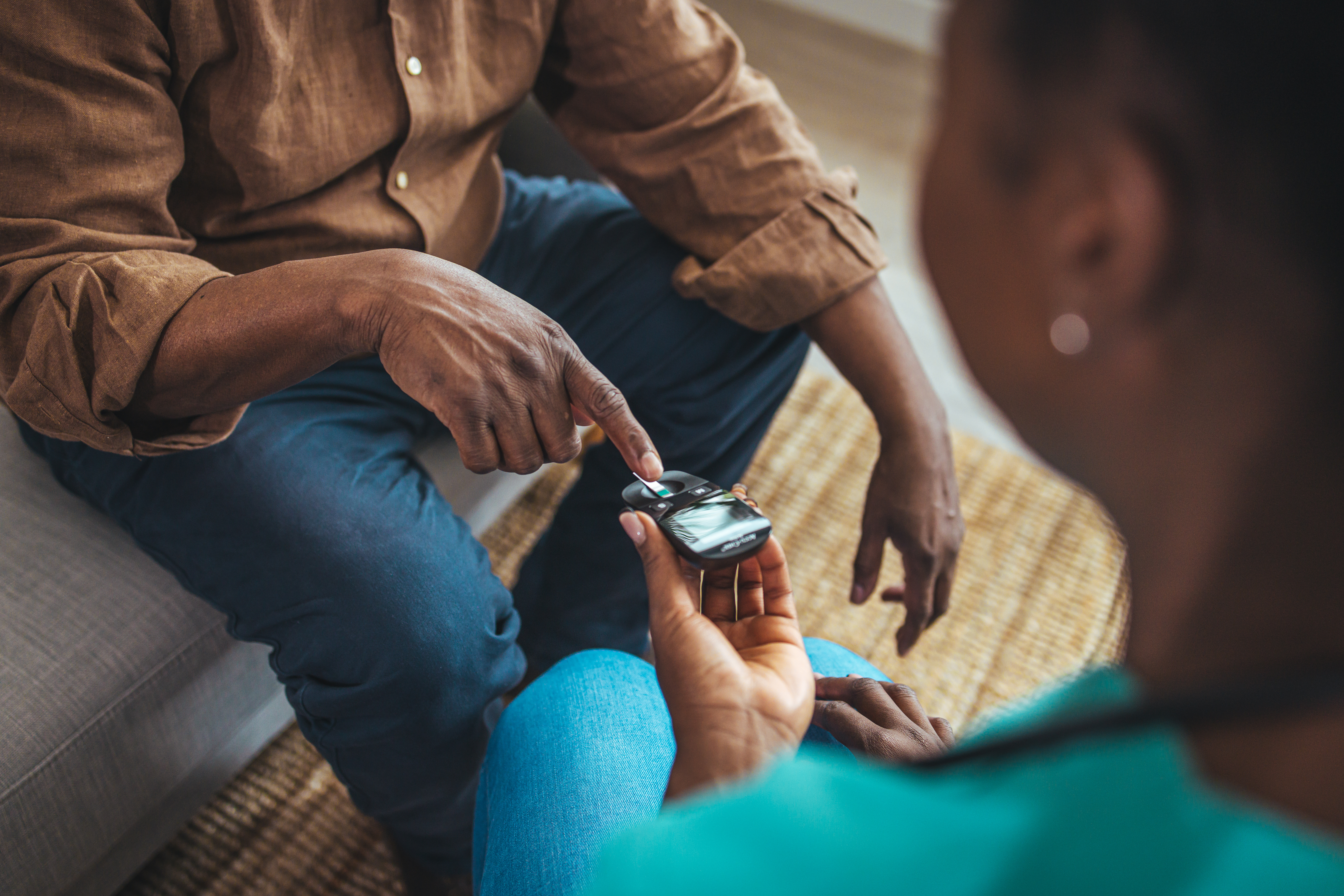 Young nurse doing a glucose blood test for diabetes on her senior male patient, during a home visit.