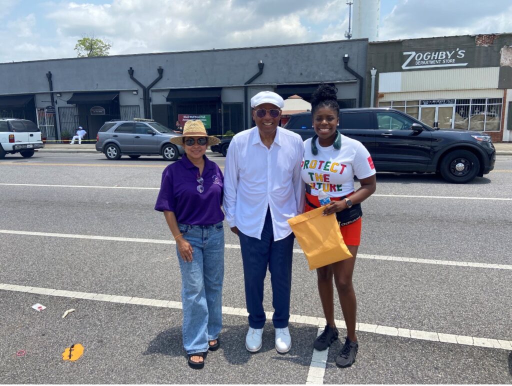 Stephanie Khat, Dr. Earl Suttle, and LaSheryl Dotch pose for a picture on the street in front of some downtown buildings in Prichard. LaSheryl is wearing a t-shirt that says "Protect the Future" and Stephanie is wearing a t-shirt from the Alabama Department of Public Health.