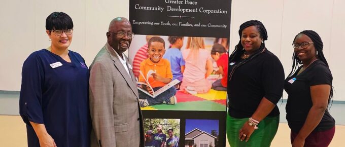 Clarinda Jones Turner, Dr. Reverend Clifford E. Jones, Regional Director Sheree Taylor, & Community Liaison Adrian Holloway pose in front of a Greater Peace Community Development Corporation sign at their workshop