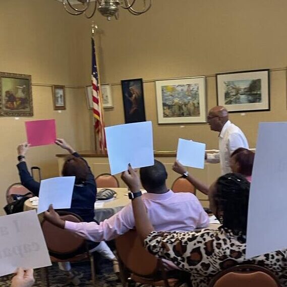 Dr. Earl Suttle leads an exercise at the Fayette kickoff. Attendees are sitting at tables and holding up sheets of paper that have empowering phrases written on them.