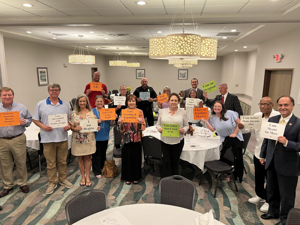 Dr. Earl Suttle leads an exercise at the Guin kickoff. Attendees are standing and posing and holding up sheets of paper that have empowering phrases written on them.