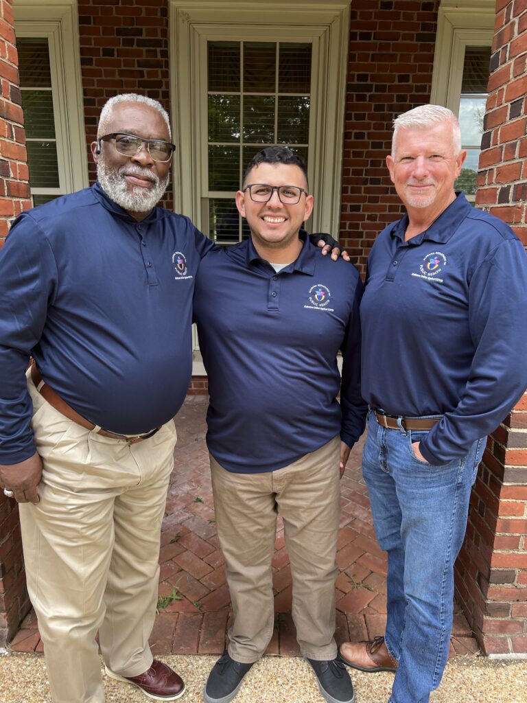 Leroy Davis, David Perez, & Keith Rhudy stand in front of a brick building wearing matching shirts from the Alabama Department of Public Health