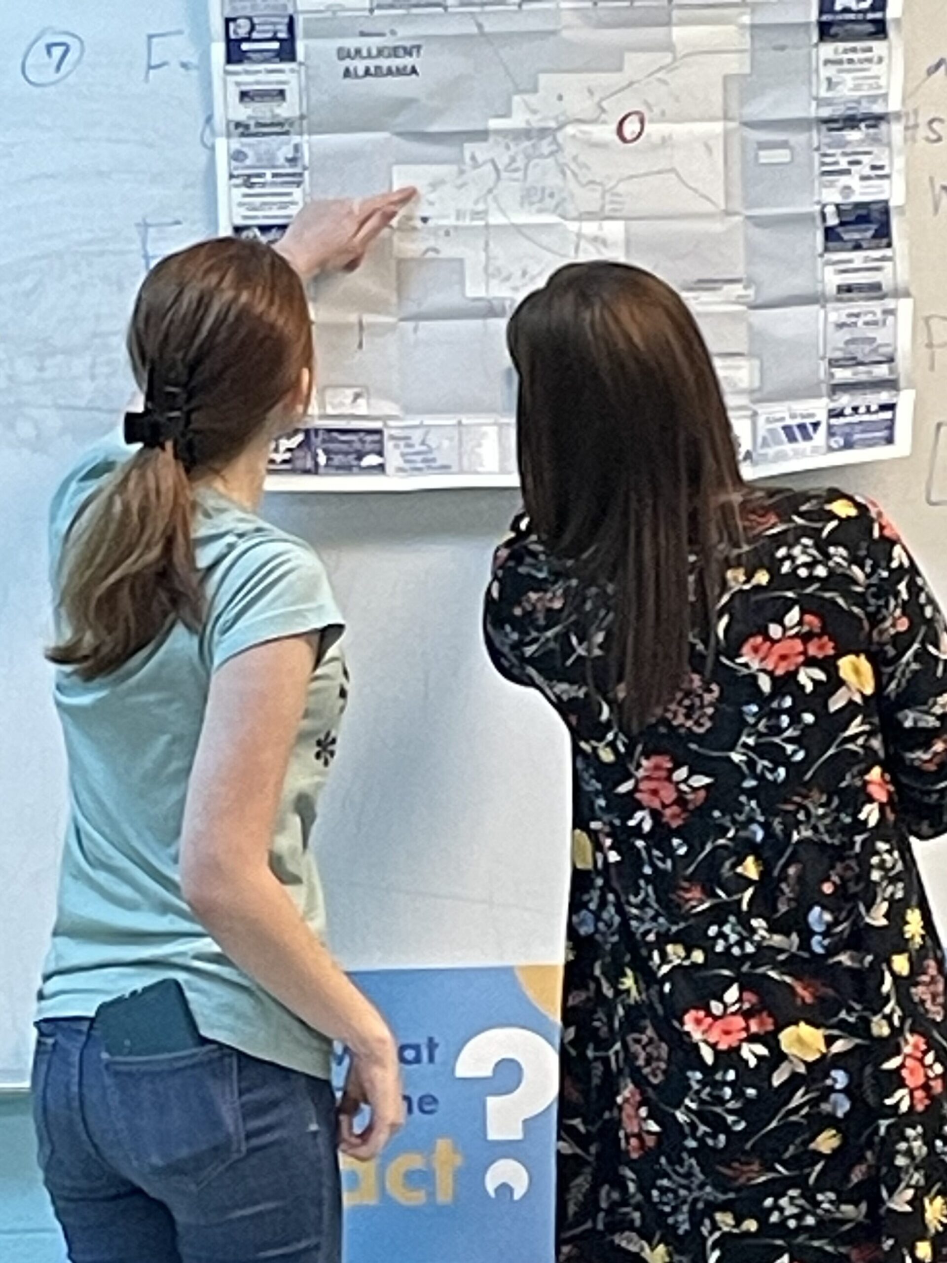 Community Liaison Kacie Long and a student look and point at a map of Sulligent handing on a whiteboard.